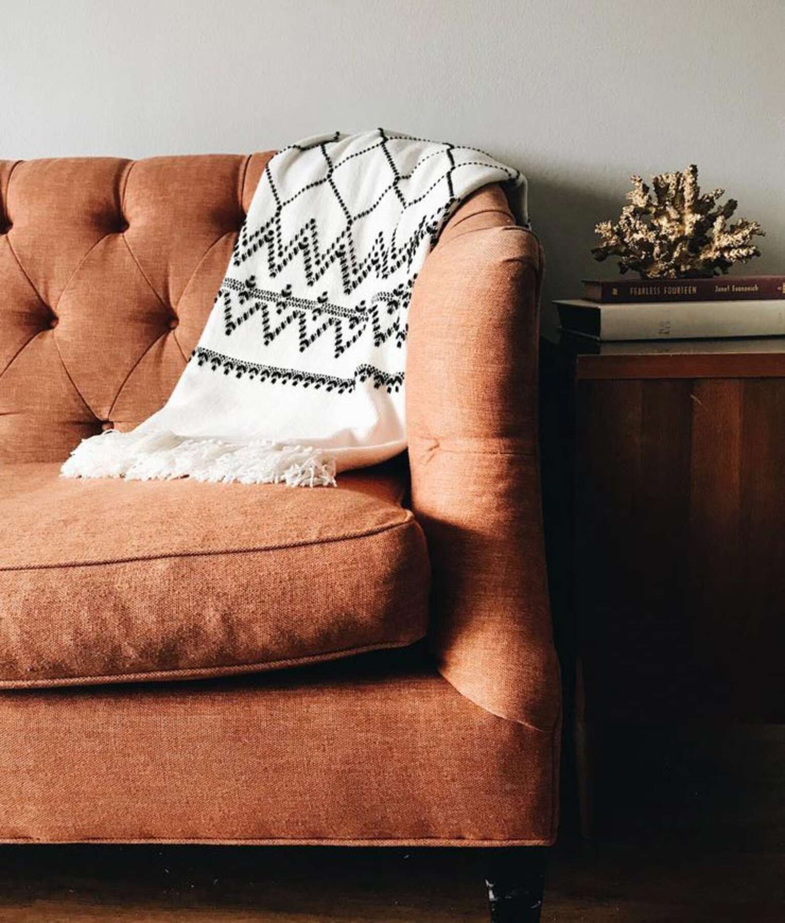 A brown couch with a blanket on top of it.